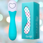 A turquoise and white OhMiBod Lovelife Cuddle G-Spot Vibrator is displayed beside its turquoise box packaging, which features a colorful, geometric design and the words "Lovelife Cuddle" by OhMiBod. The background is softly blurred with circular light spots, creating a gently illuminated scene that suggests personal pleasure and targeted sensations.